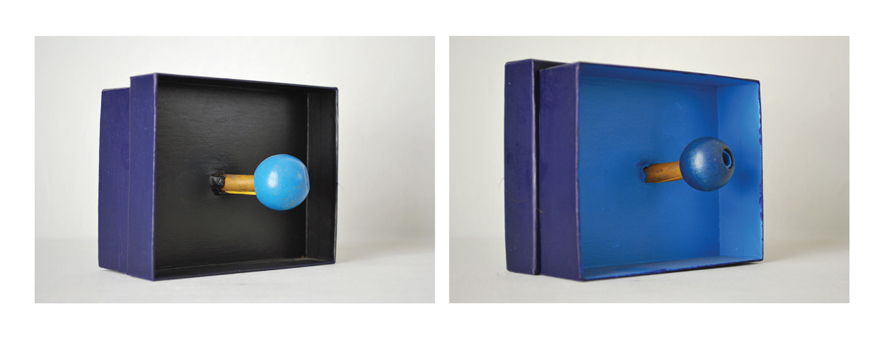 Wormhole by Arthur Bruso. Back and front of an open box, one side black and one side blue, each with a blue knob on a short rod, against a white background.