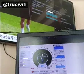 โน้ตบุ๊กแสดงผลทดสอบความเร็วอินเทอร์เน็ต True Online และสัญญาณไวไฟทาง โทรทัศน์ที่อยู่ด้านหลัง