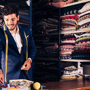 Tailor in blue suit with measuring tape arranging colorful sewing supplies in fabric shop