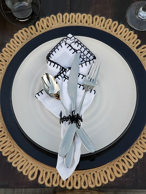 Elegant table setting with a white plate, black-trimmed white napkin, black "Thankful" napkin ring, black charger plate, and