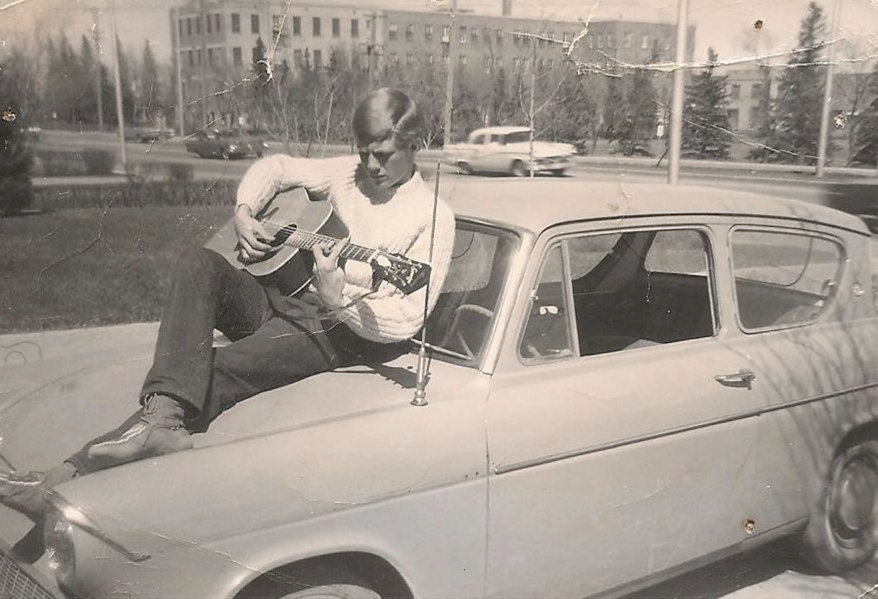 Man plays guitar on the roof of his car in a sepia photograph