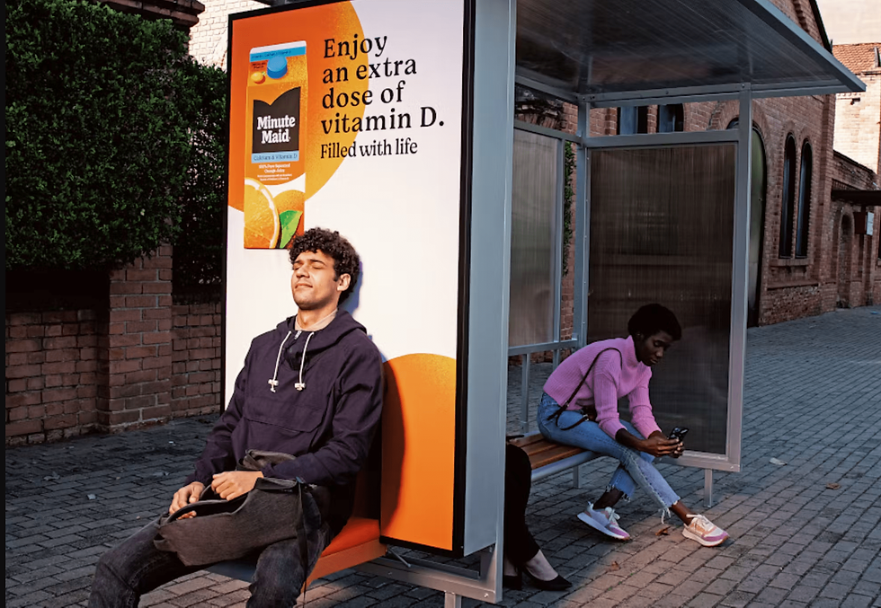 A man sitting at a bus shelter OOH ad underneath an ad. 