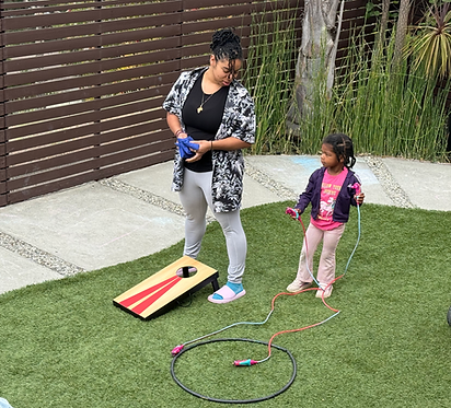 A staff member playing outdoor games with child at Oakland Community Motessori School, a Montessori preschool and daycare serving children 18 months to five years old in Oakland and the surrounding Bay Area.