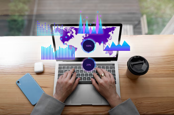 Hands typing on a laptop with a world map and digital charts on screen. Nearby are a smartphone and coffee cup on a wooden desk.