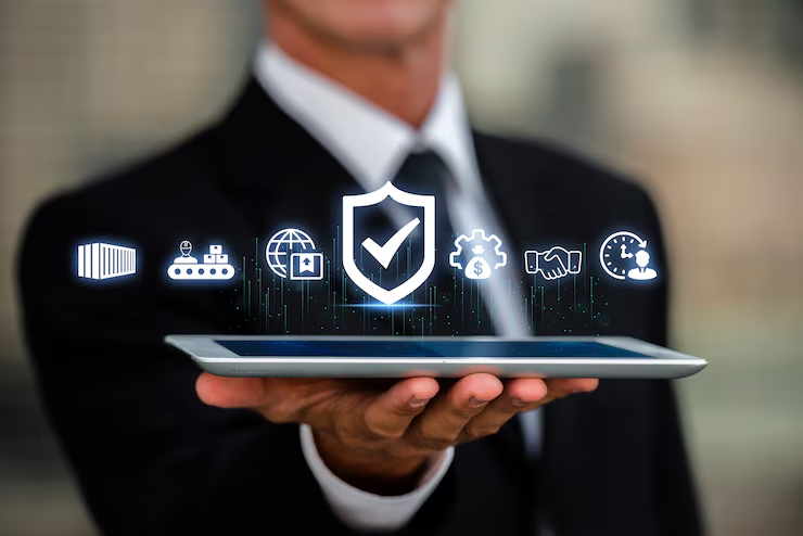 A person in a suit holds a tablet with floating digital icons including a shield, gear, and globe. The scene is professional and futuristic.