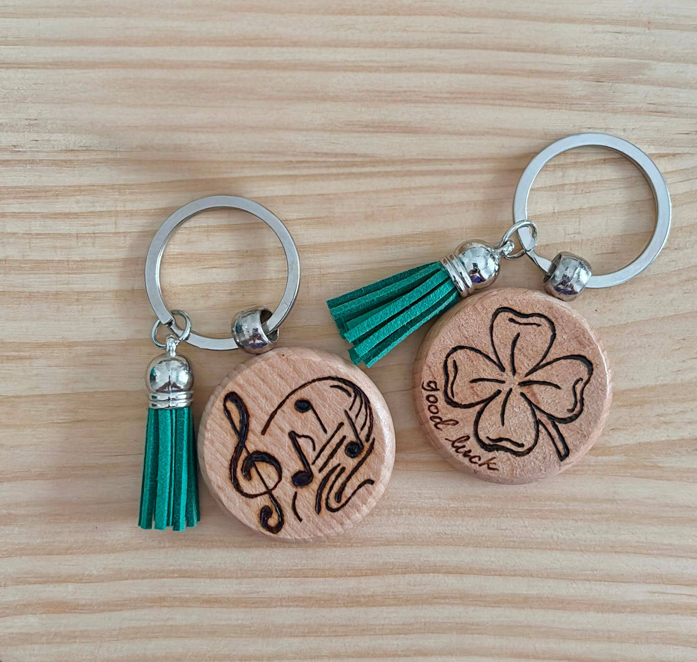 Portachiavi tondi in legno pirografati a mano con nappe verdi raffiguranti note musicali e un quadrifoglio.
