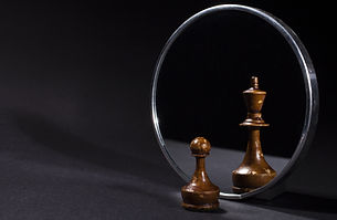 Pawn looking in the mirror and seeing a king. Black background.