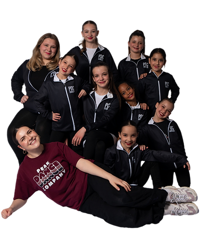 A group of young dancers from Peak Dance Company pose together in matching black and white PDC tracksuits, smiling proudly. One of their instructors lies in front, wearing a burgundy Peak Dance Company T-shirt and black pants, smiling warmly at the camera. This joyful group portrait captures the spirit of community, confidence, and pride at Peak Dance Company, a premier dance studio in Niagara-on-the-Lake.