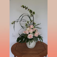 Delicate floral arrangement with pale pink roses, greenery and blooming branches in a ceramic pot