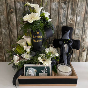 White sympathy flower arrangement with calla lilies, white gerberas, a memorial candle and a decorative cross.