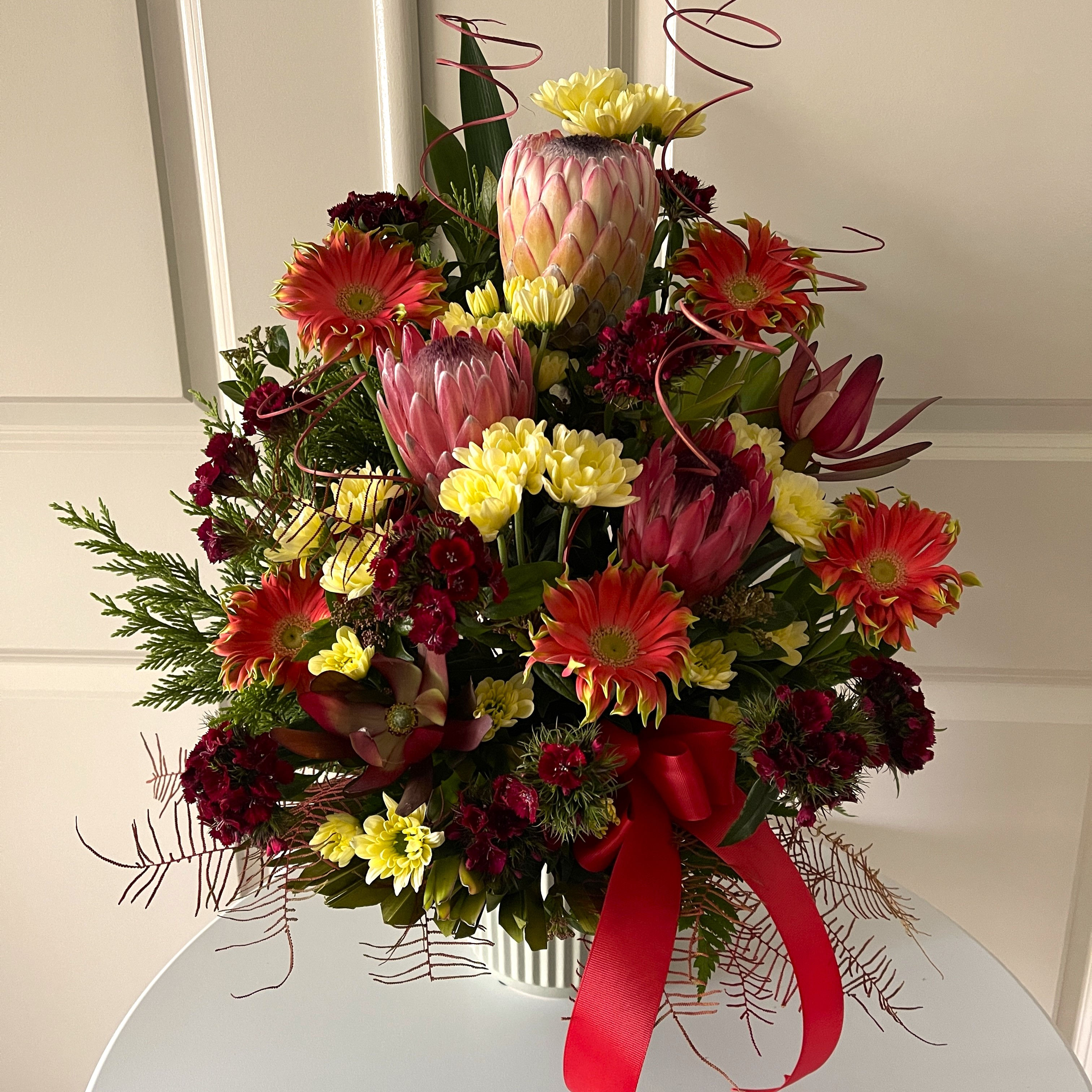 Bushland Blooms flower arrangement in rich red tones with native-inspired flowers in a ceramic pot.
