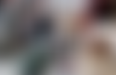Man serves two people at rustic cafe with wooden tables. Industrial decor, soft light, empty chairs in foreground, casual mood.