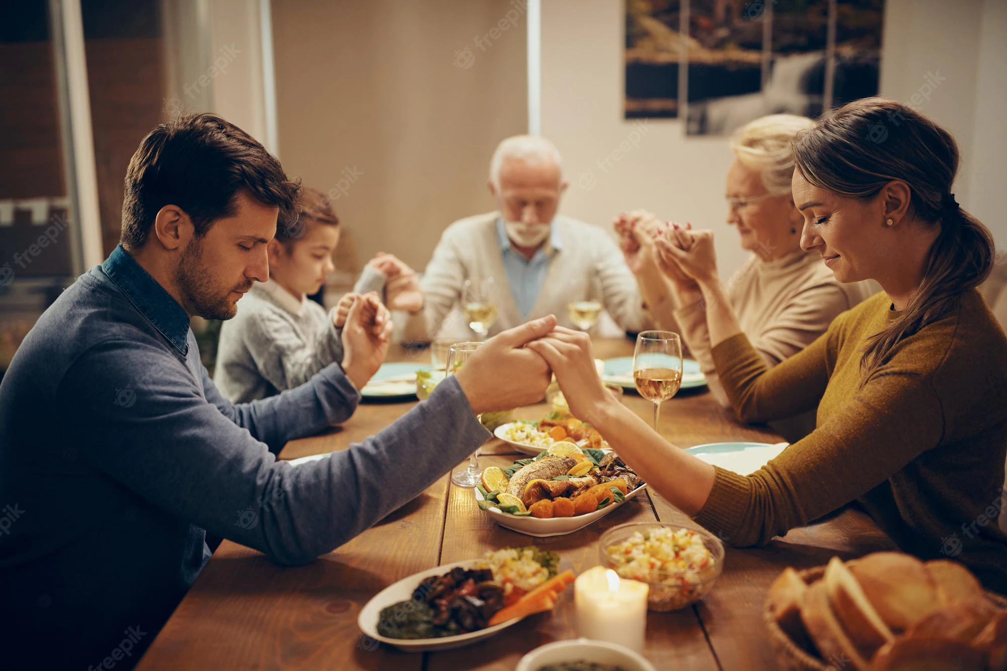 multigeneration-family-holding-hands-praying-during-lunch-dining-room_637285-12557.webp