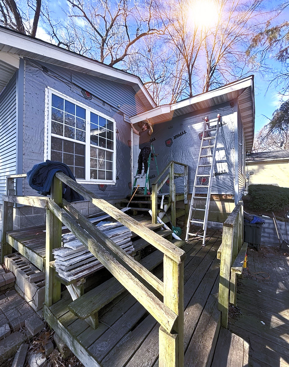 House exterior under renovation with siding, ladders, and worker