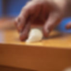A sushi chef’s hand placing fresh nigiri onto a wooden counter aboard guntû.