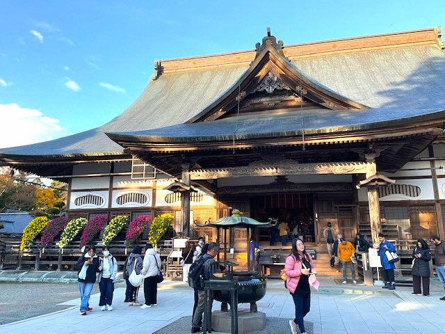 The main hall of Chuson-ji temple in Hiraizumi Japan a large wooden structure with chrysanthemum arrangements at the entrance and visitors in the foreground