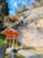 The Ganmen Daibutsu Northern Rock Buddha carved into the sandstone cliff face at Takkoku no Iwaya Hiraizumi Japan with a small vermilion shrine structure below