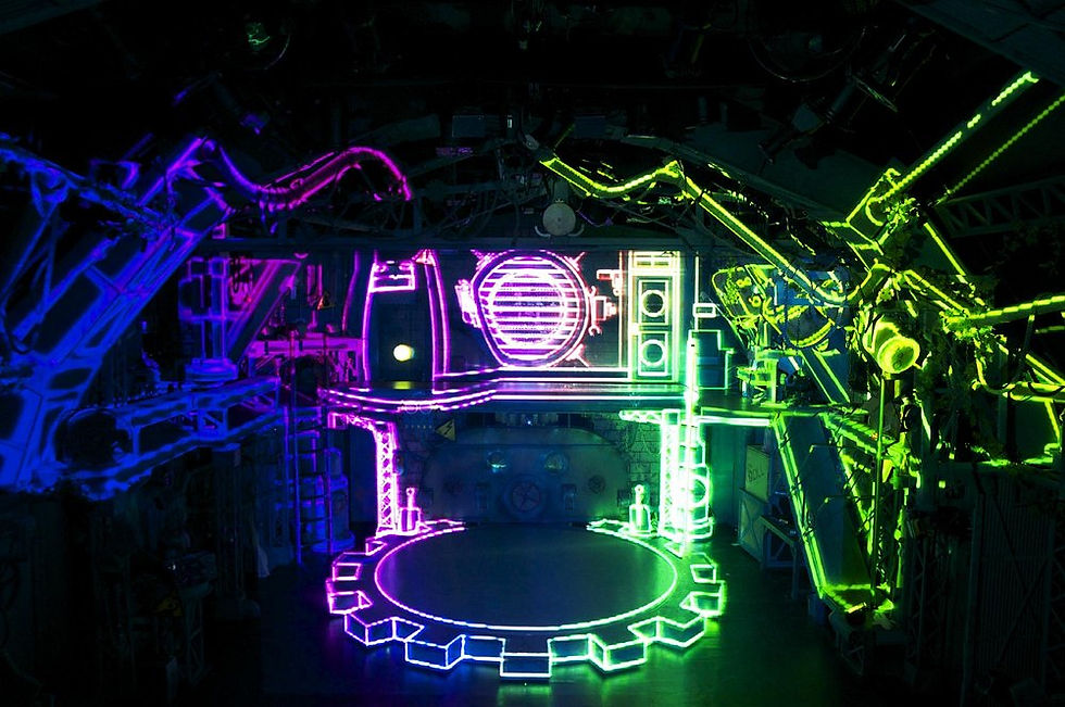 GEAR Kyoto empty stage illuminated in vivid neon pink, blue, and green lighting revealing the full steampunk industrial set desig
