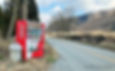 Red vending machine standing alone beside a quiet rural road in Japan, with open fields, bare trees, and low mountains in the background