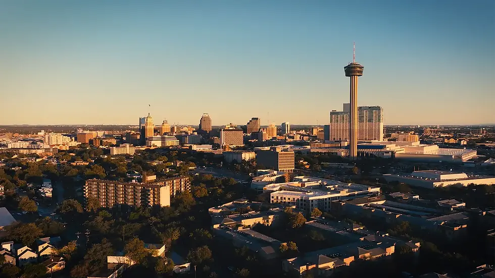 Golden-hour city skyline with a tall observation tower above buildings and trees under a clear blue sky.