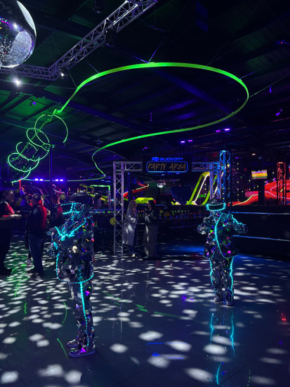 Indoor park with people dressed in robot outfits and lights shining on floor
