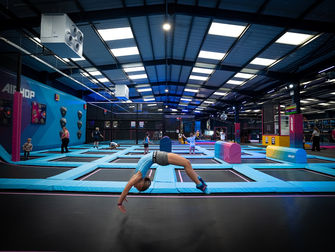 Girl in leotard doing back flip on trampoline bed in large trampoline park