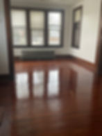 An image of an empty room with polished hardwood floors and a large window, offering a serene view.