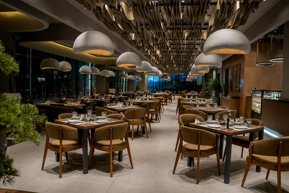 Elegant restaurant interior with brown tables set for dining. White dome lights hang from a patterned ceiling. Relaxed, inviting atmosphere.