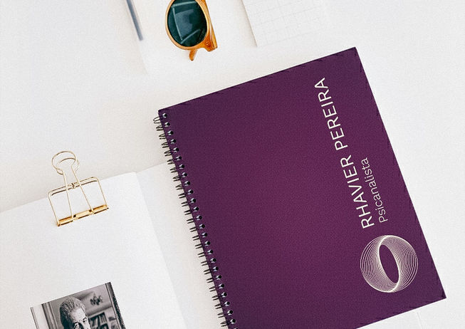 Caderno roxo, caneta dourada e óculos em composição de luz e sombra.