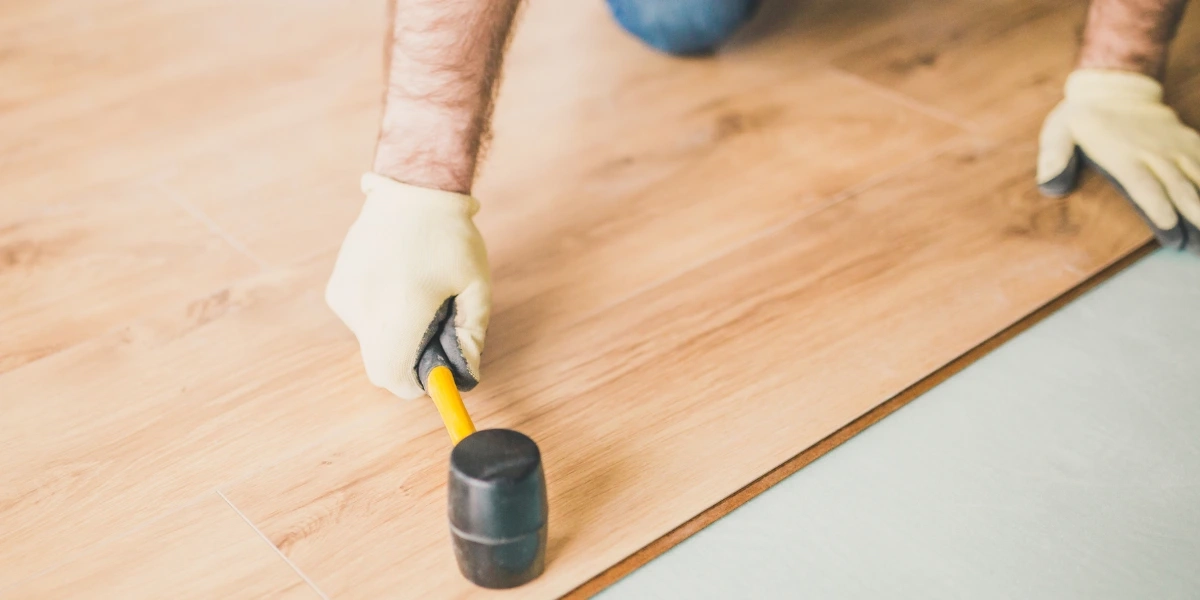 A person using a rubber mallet to attach laminate planks to the tile surface