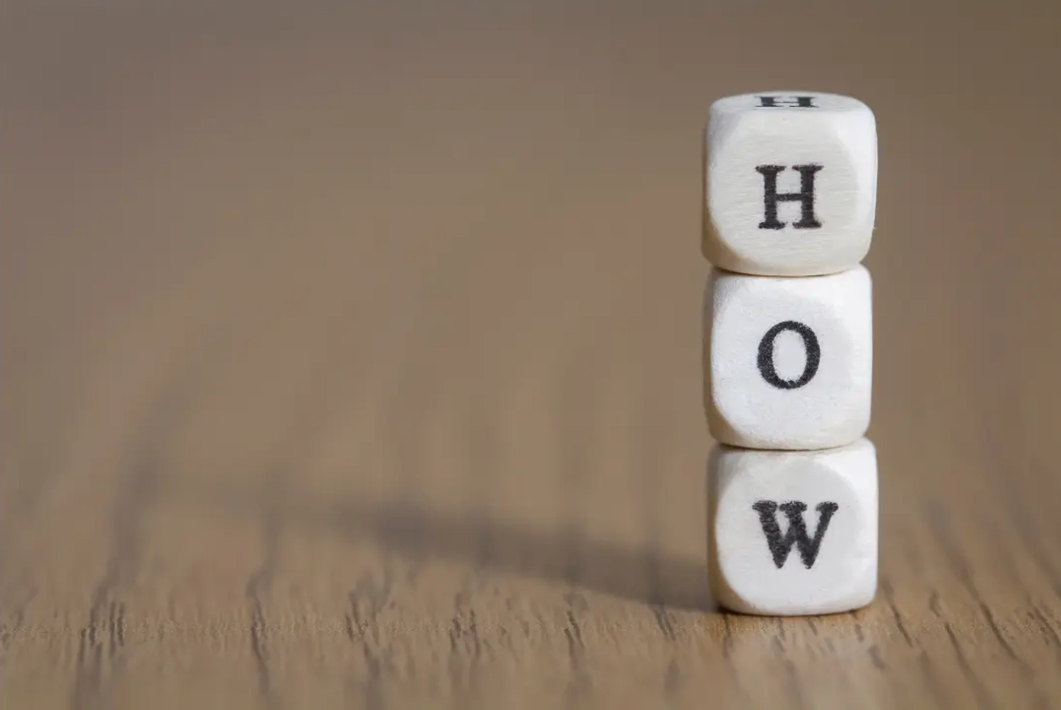 A stack of wooden cubes with the word "HOW" printed on them.