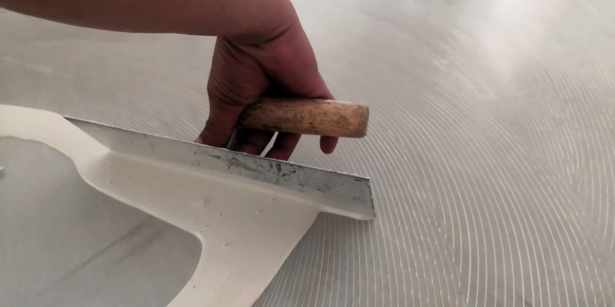 A person using a floor scraper to level the tile surface for laminate installation, answering the question 'Can you put laminate over tile?'