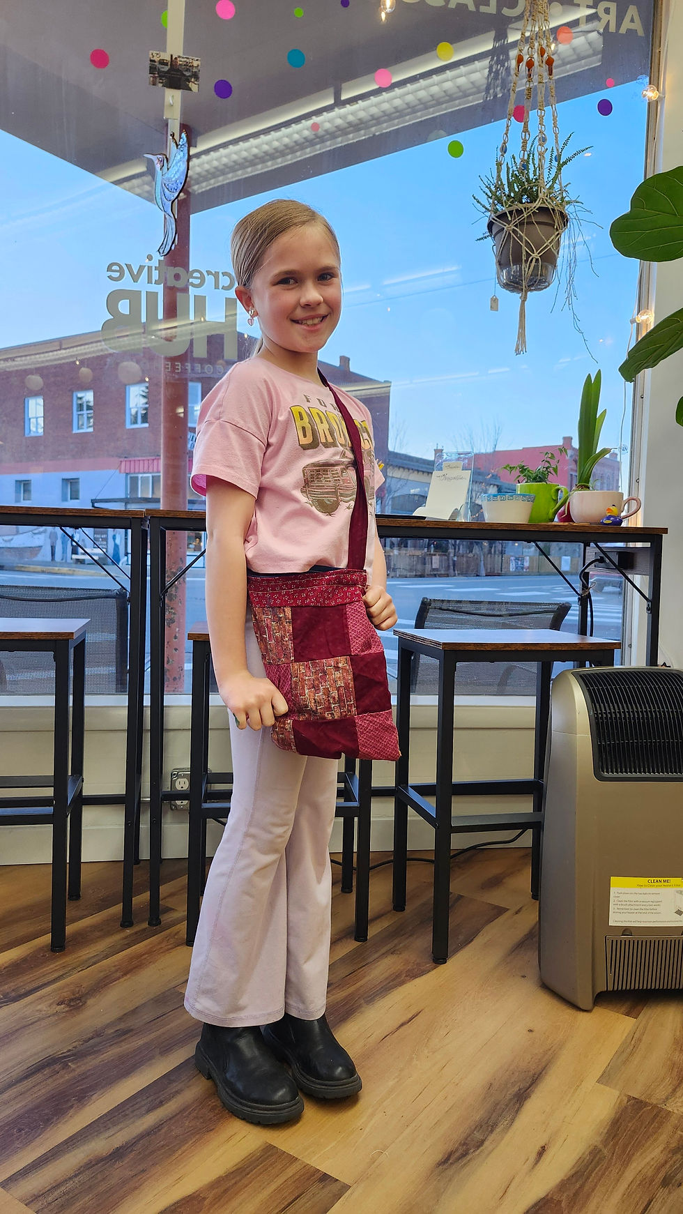 Happy child beaming with pride, holding up a handmade bag, showcasing creative accomplishment and self-astonishment from a sewing workshop.