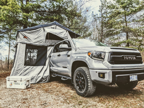 A rooftop tent setup with its annex room and a cooler