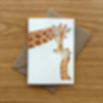 A greeting card with a Giraffe Mother and Baby on the front, displayed on a Kraft brown envelop
