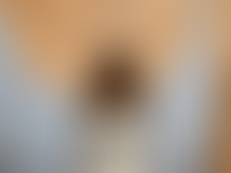 A close-up of a single hand holding an amber glass serum bottle labeled "Aesthetic Marketing" with a dropper suspended above it. The label features bold black text listing phrases like “Conversion Booster Serum,” “Scalable Growth,” “Patient Journey Optimiser,” and “Lead Magnet Elixir.” The background is softly blurred, with a person wearing a light blue top partially visible, creating a clean, professional, and elegant aesthetic.