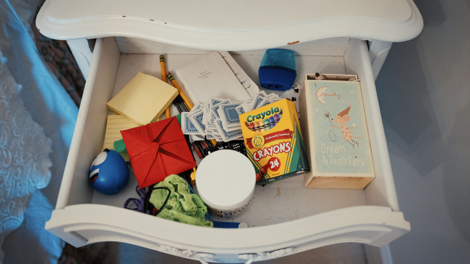 Looking down at the content of a drawer, including crayons, playing cards, notes, pencils, and more.