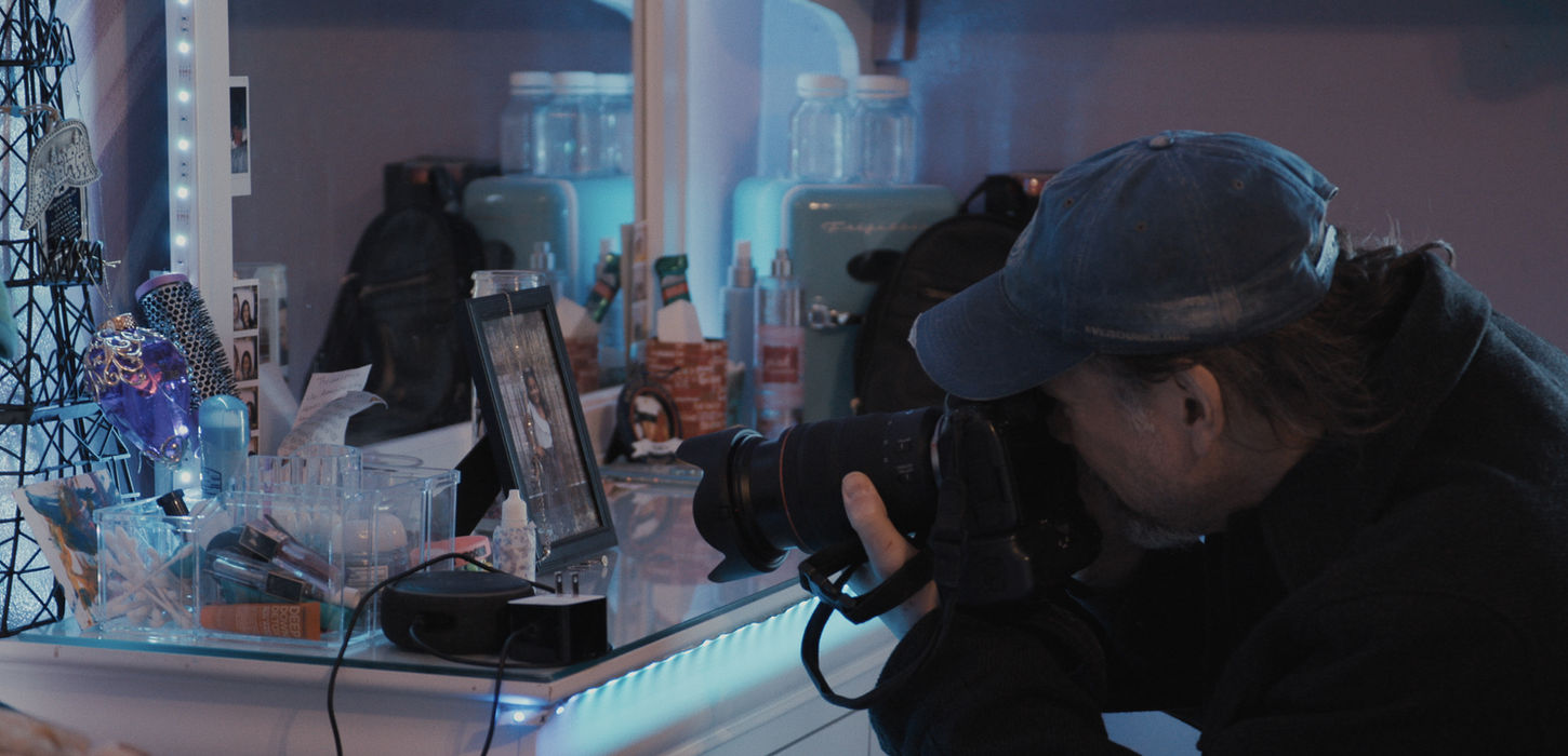 Photographer Lou Bopp photographs items on a white vanity lit by blue LED lights.