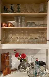 Organized bar cabinet with variety of specialty drink glasses, wine glasses, craft beer glasses, copper mugs, margarita glasses, martini glasses, beer steins, champagne flutes, shot glasses. Counter top with win holder and bar tools