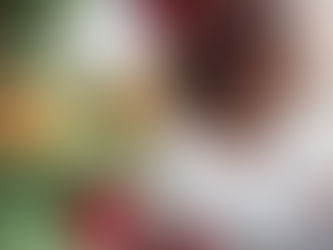 Woman in glasses gazes out a window, wearing a white shirt, with a decorated Christmas tree featuring red and gold ornaments nearby.