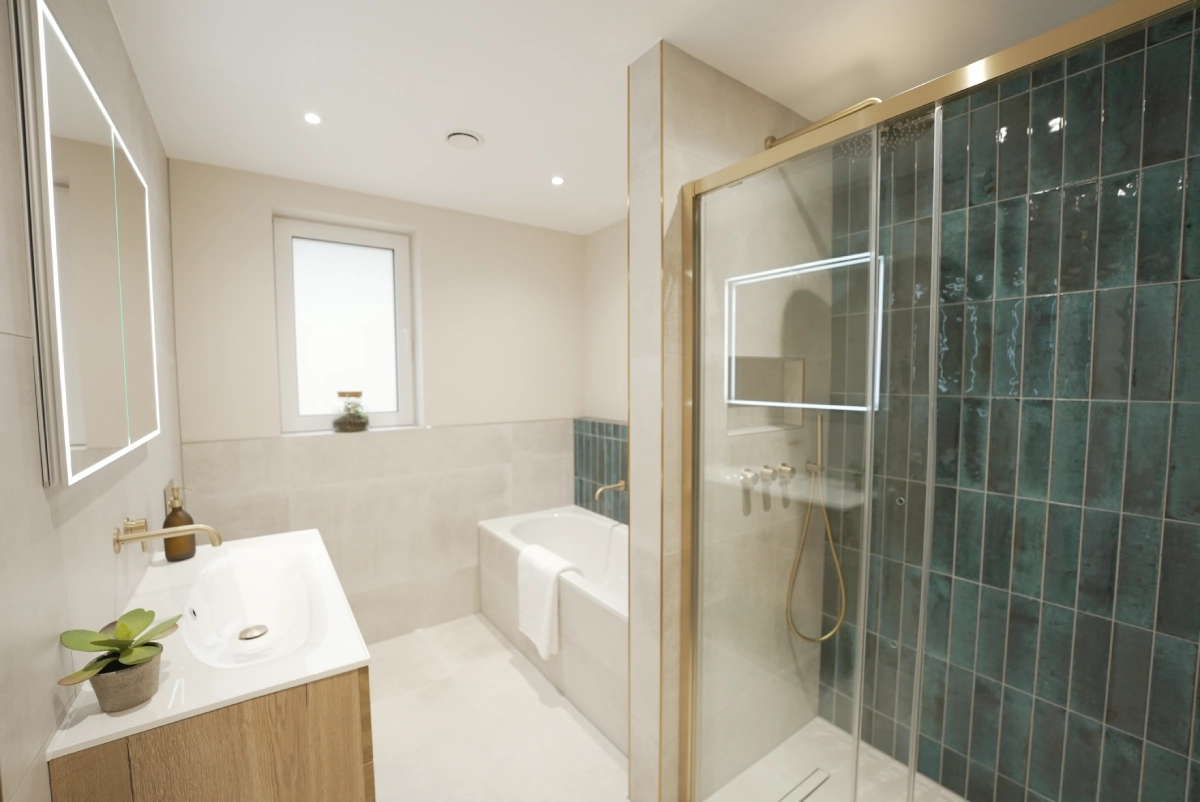 Modern bathroom with a glass shower and teal tiles, a bathtub with a white towel, and a wooden vanity holding a small plant. Bright and minimalist.
