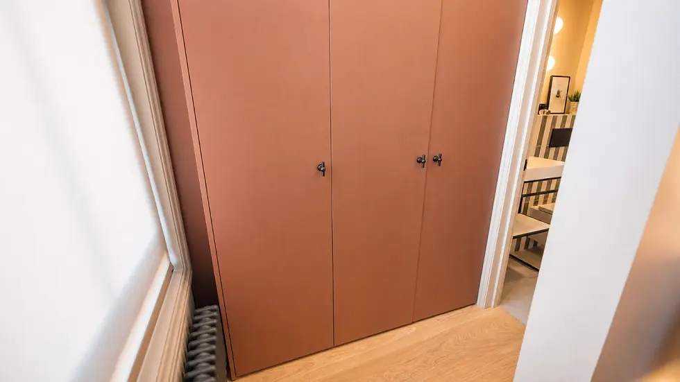 Narrow hallway with large brown closet doors, wood floor, and a glimpse of a lit bathroom with striped tiles and sink.
