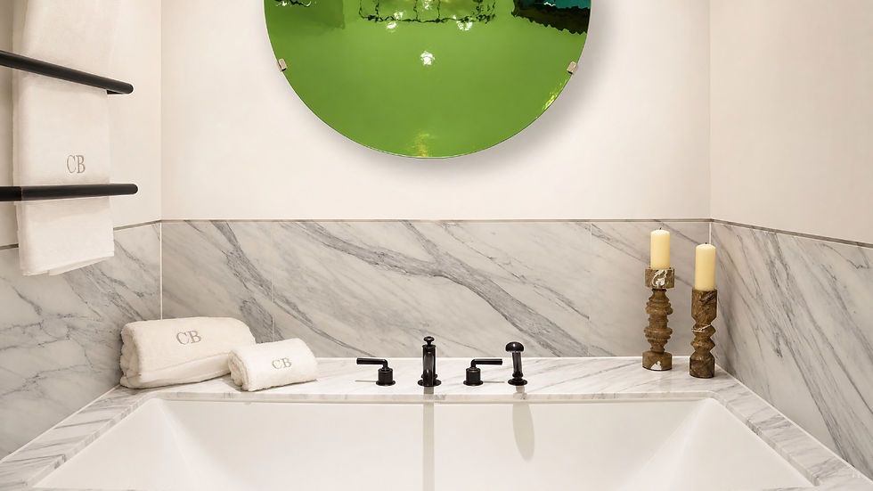 Luxury marble bathroom with a white tub, CB towels, candles, and a large green round mirror above.