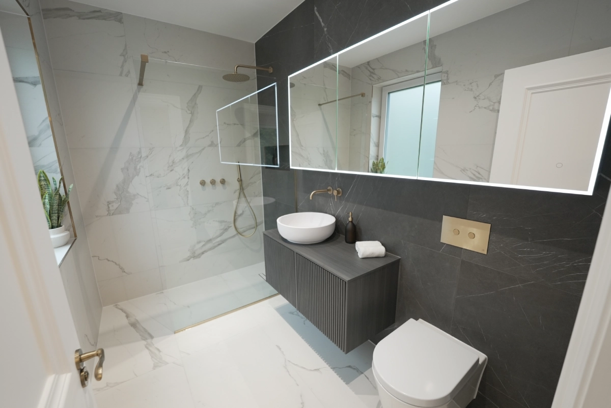 Modern bathroom with a walk-in shower, marble walls, and floor. Features include a large mirror, vessel sink, sleek toilet, and minimalist decor.