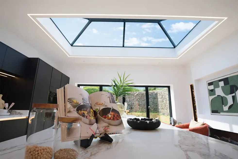 Modern kitchen with skylight, marble island with open cookbook, jars, and plant. Black cabinets, window view, abstract wall art.