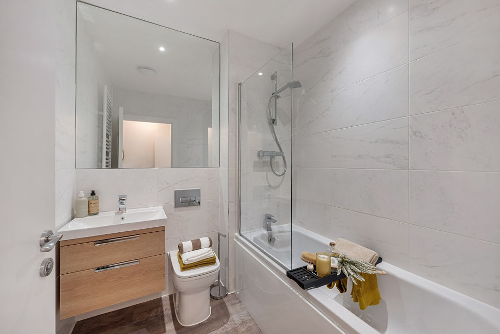 Modern bathroom with white tiles, bathtub with glass screen, wooden vanity, and mirror. Neatly arranged towels and toiletries add a cozy touch.