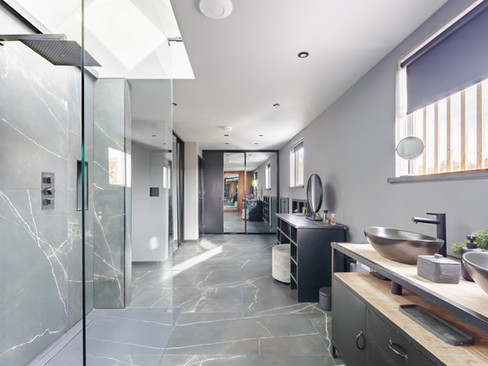 Spacious contemporary bathroom with large-format grey marble-effect tiles, walk-in rainfall shower, double vessel sinks on a wood vanity and recessed ceiling lighting.
