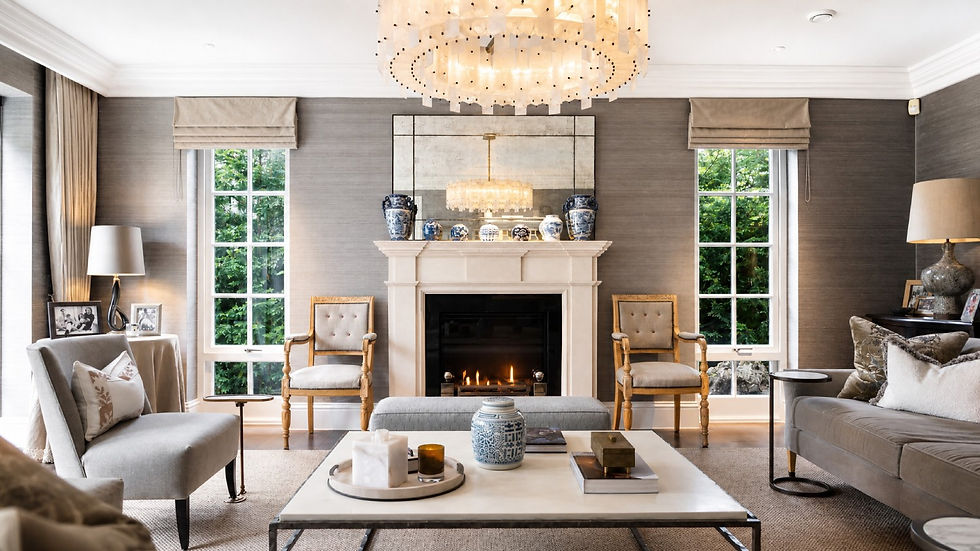 Elegant living room with lit fireplace, chandelier, gray sofas and chairs, blue-and-white vases, and green garden views through tall windows