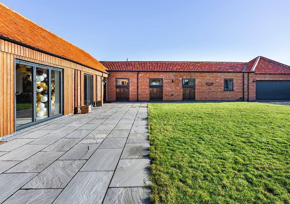 Brick building with red roof, large windows filled with balloons. Stone patio and green lawn under clear blue sky. Calm and inviting setting.