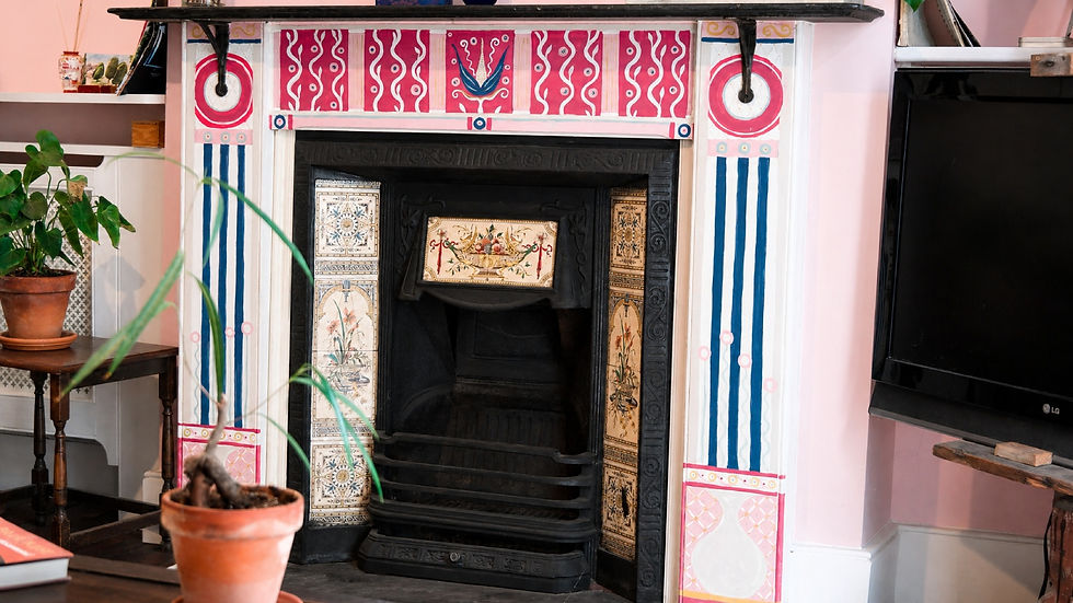 Decorated fireplace with pink-and-blue painted mantel, potted plants nearby, and a black TV in a cozy room.